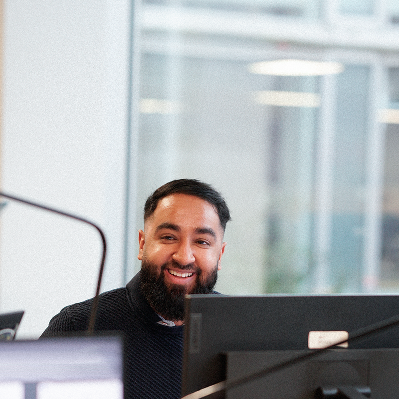 Hamza sidder foran sin pc og smiler til kollega