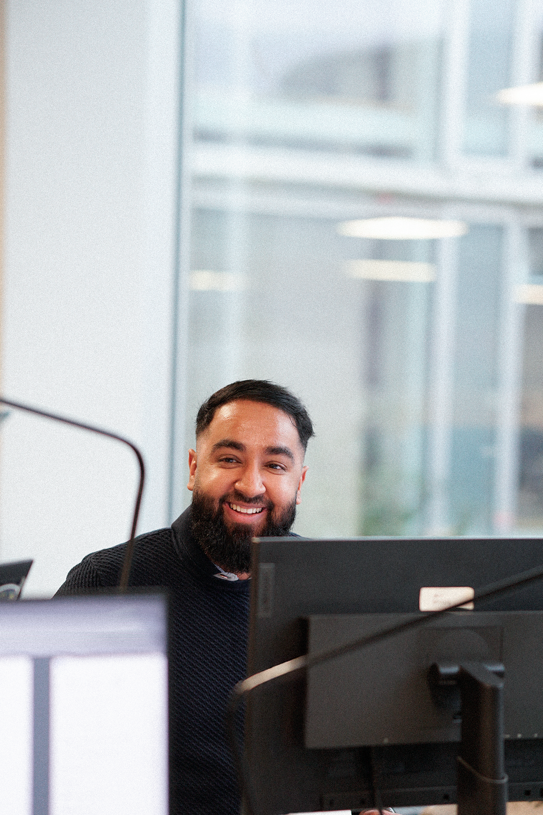 Hamza sidder foran sin pc og smiler til kollega